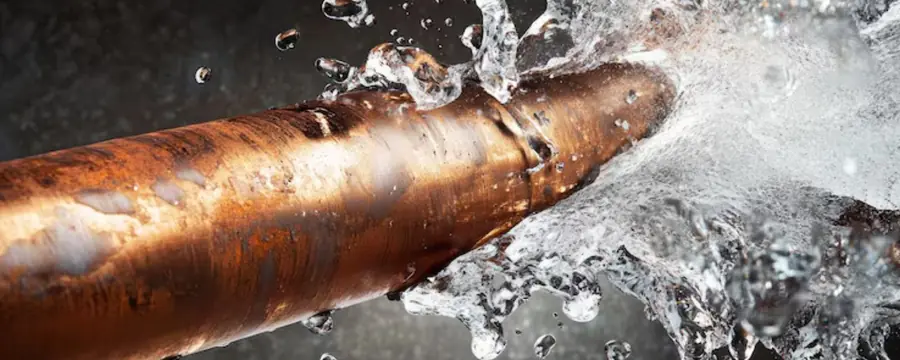 A split copper water pipe sprays water outward.