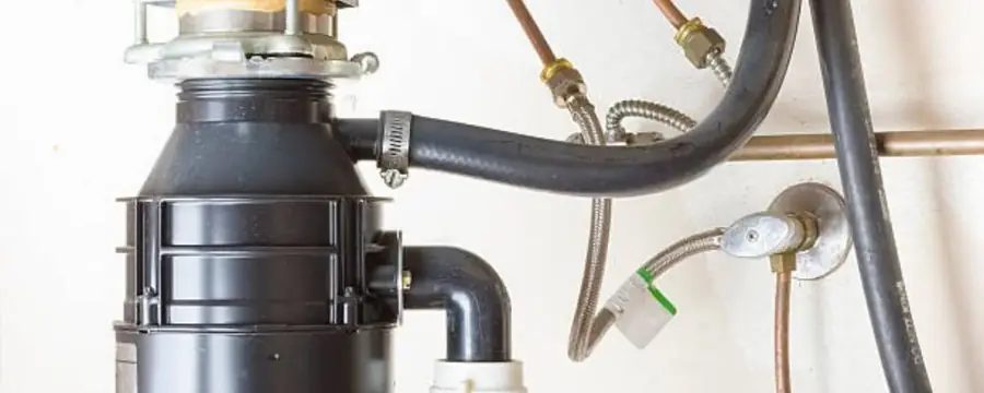 A garbage disposal mounted under a kitchen sink with its drain hose and wiring.