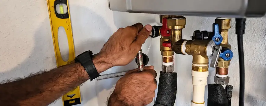 Hands fit service valves on the plumbing below a wall-mounted tankless water heater, with a level on the wall.
